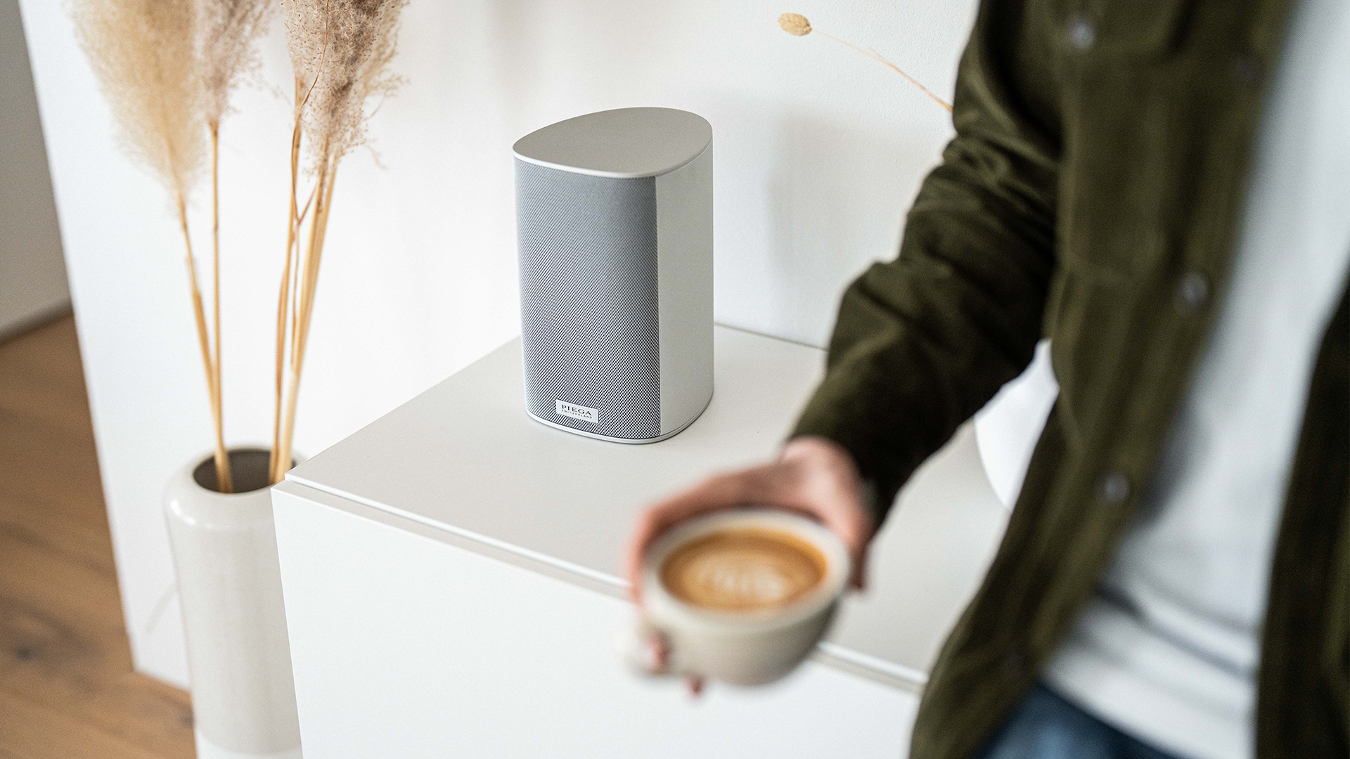 Ein Ace 30 Wireless Speaker steht in einer modernen Wohnung mit einer Person, die gerade Kaffee geniesst.